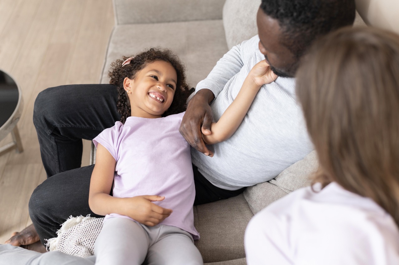 Father and daughter laughing together on couch during parent coaching session with Dr. Celeste Jones PsyD